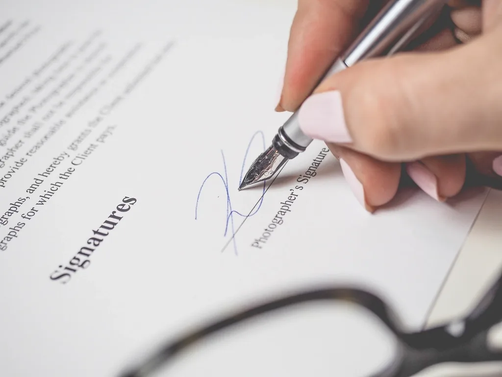 A hand signing a document labelled 'Signatures' with a silver fountain pen